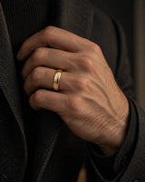 Man wearing a polished gold tungsten wedding ring with a rounded court profile while adjusting a dark tailored jacket.