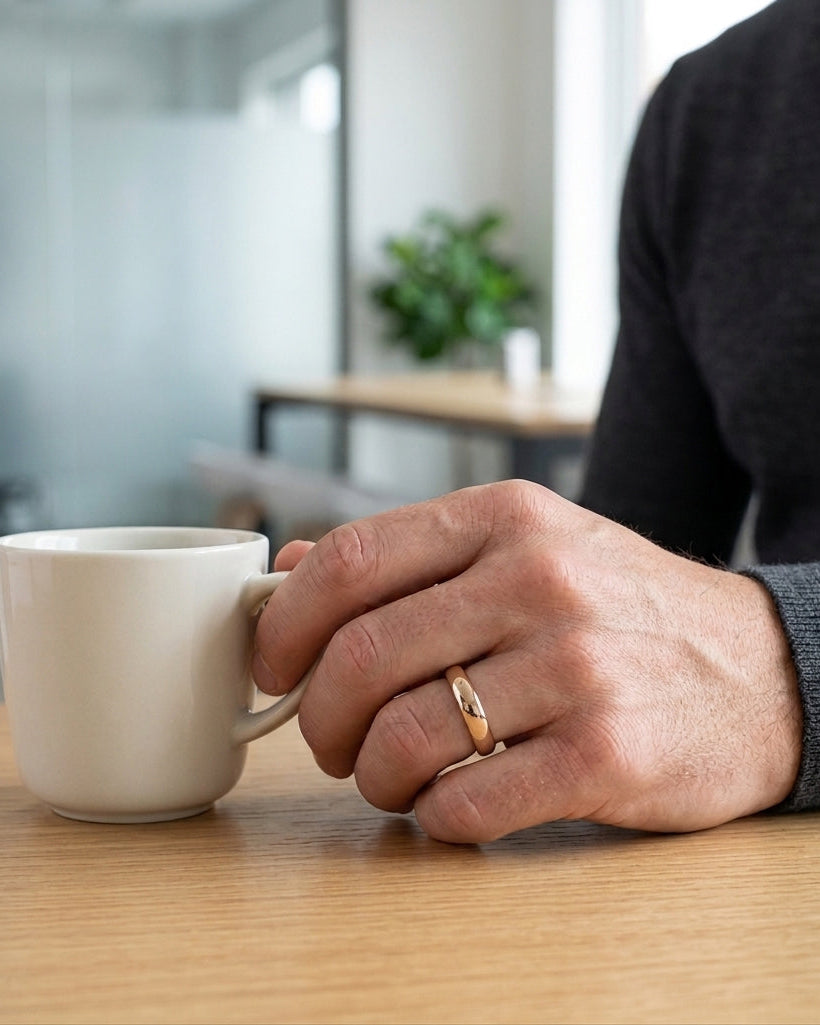 Person holding a beige mug on a wooden table with a blurred office background