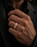 Man wearing a polished rose gold tungsten wedding band while adjusting his dark jacket, showing the smooth rounded profile and reflective finish.