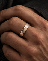 Close up of a man's hand wearing a polished rose gold tungsten wedding ring with a rounded court profile against dark clothing.
