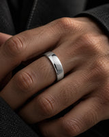 Close up of a polished silver tungsten wedding ring with a smooth domed profile, worn on a man's ring finger against a dark background.