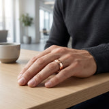 Hand wearing a rose gold ring on a wooden table with a blurred indoor background