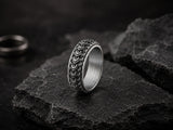 Silver dragon scale textured men’s wedding ring on dark volcanic rock with moody cinematic lighting and rugged charcoal slate background.