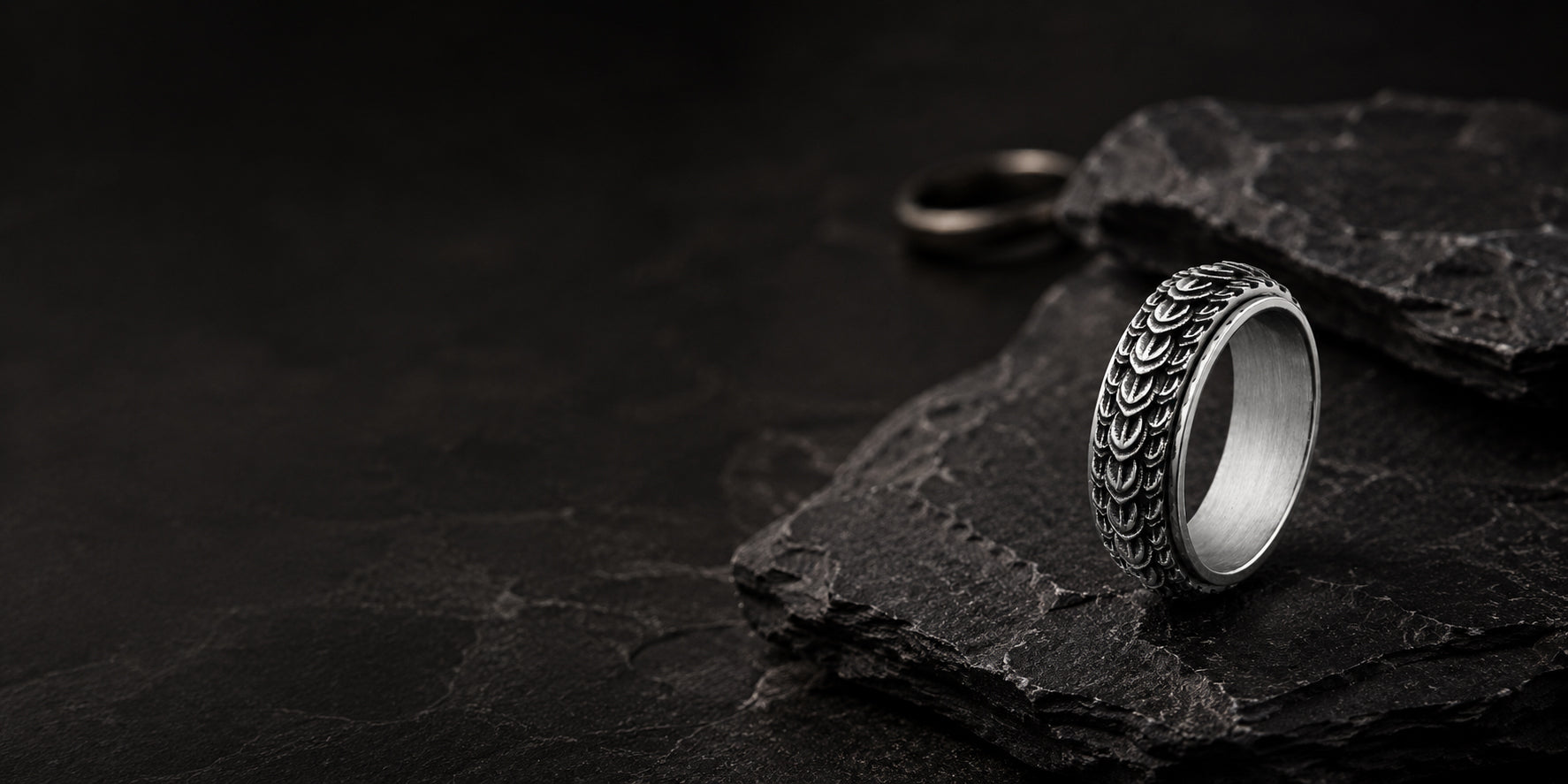 Luxury men’s dragon scale wedding ring displayed in a dark cinematic hero banner scene with rugged stone textures and premium masculine styling.