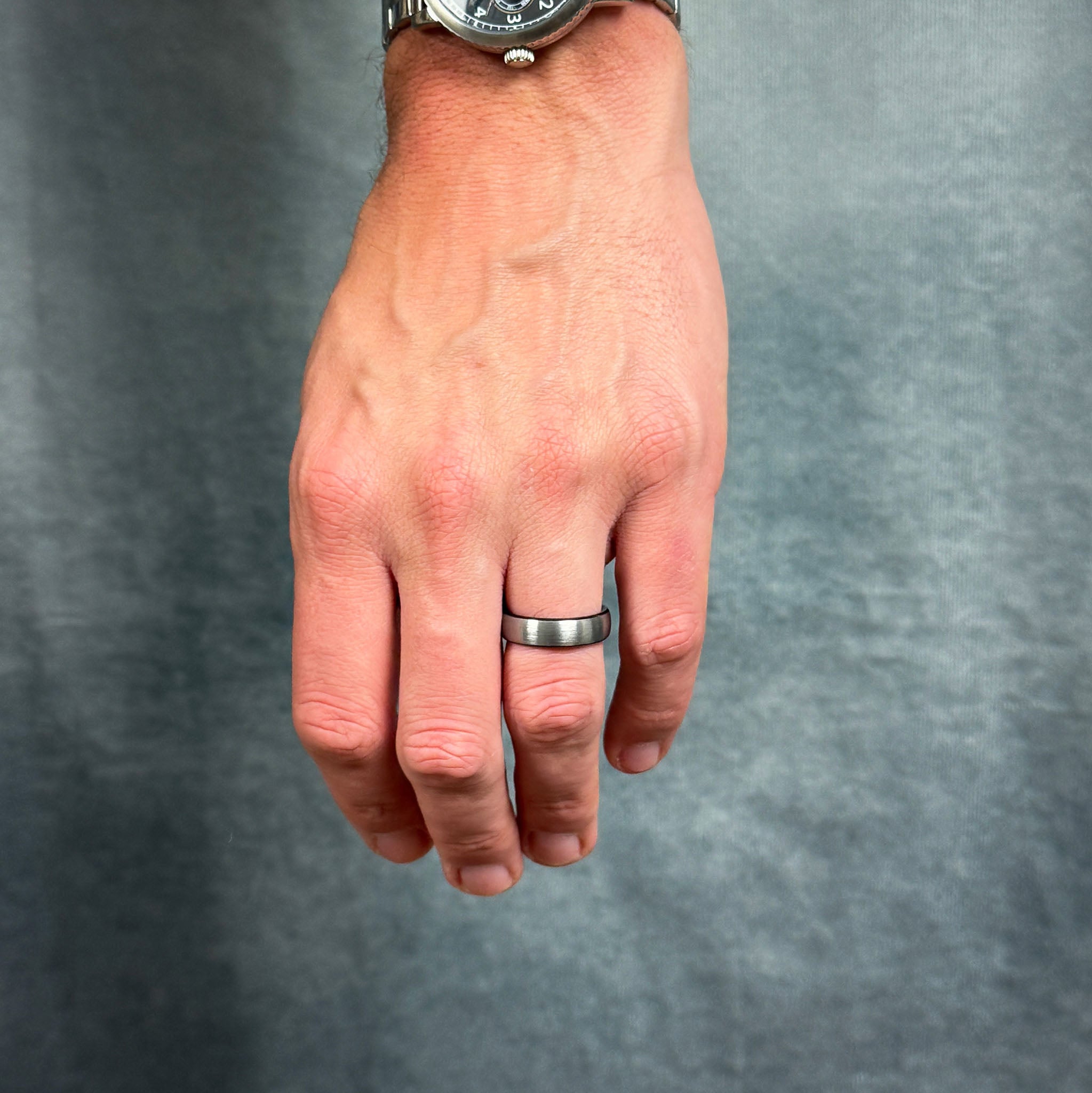 Hand wearing a silver ring on a gray background