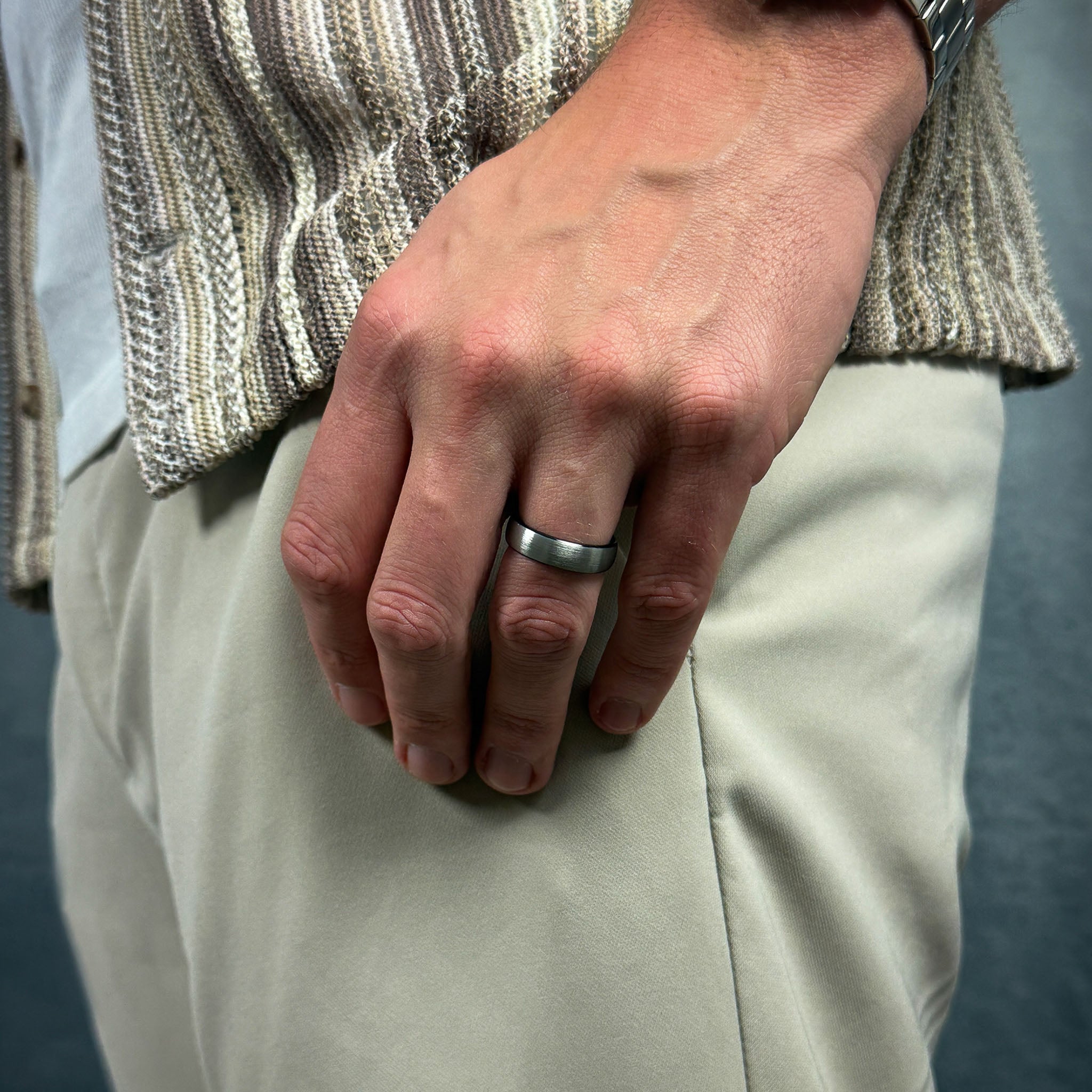 Close-up of a person's hand wearing a silver ring with a neutral background