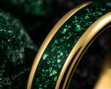 Ultra close-up macro photograph showing the detailed emerald green crushed gemstone inlay and polished gold edges of a luxury tungsten wedding ring.