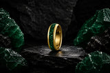 Luxury emerald wedding ring collection hero image featuring a polished gold tungsten ring with deep green crushed emerald inlay on a dark cinematic stone background.