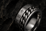 Macro close-up of a silver rune spinner ring with chain detail on dark stone background.