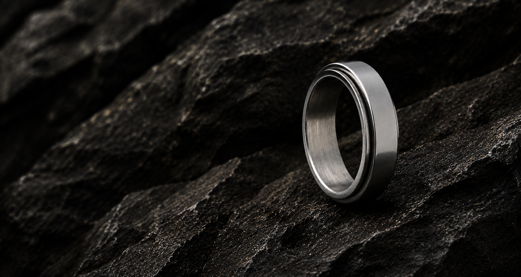 Fidget ring collection hero image featuring a silver stainless steel spinner ring on dark textured rock with cinematic lighting.