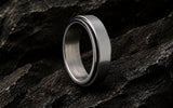 Fidget ring collection hero image featuring a silver stainless steel spinner ring on dark textured rock with cinematic lighting.
