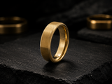 Macro close-up of brushed gold men’s wedding ring resting on dark slate showing polished edges and durable everyday design