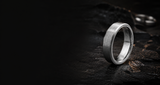 Close-up of brushed gunmetal tungsten wedding ring on dark stone showing durable textured finish and polished edges
