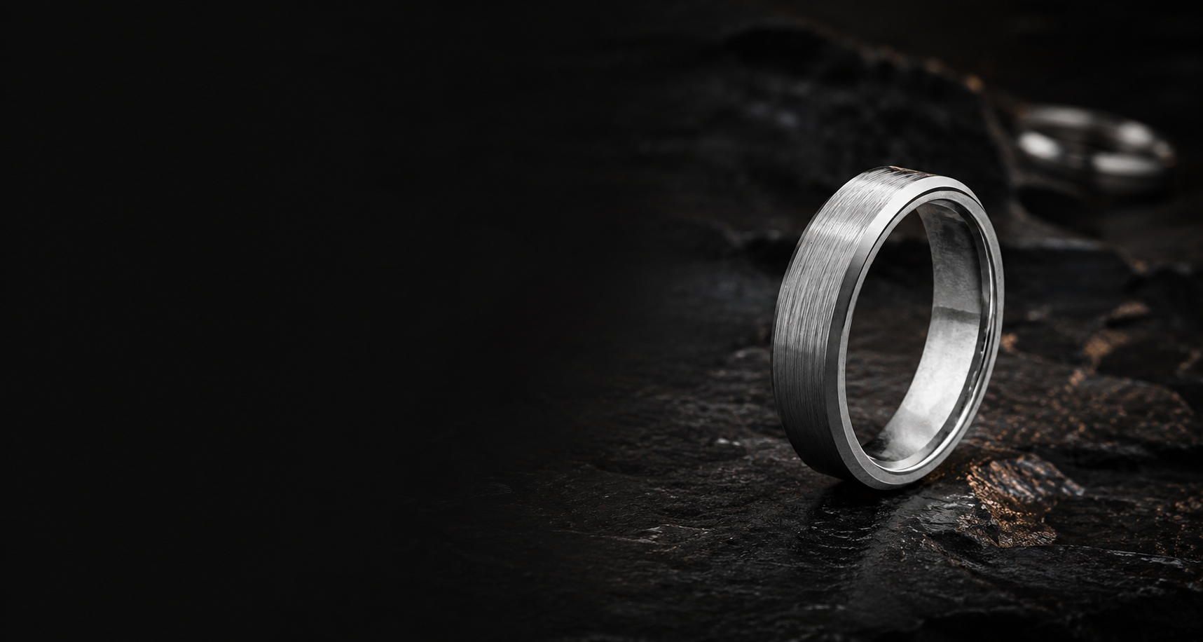 Close-up of brushed gunmetal tungsten wedding ring on dark stone showing durable textured finish and polished edges