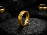Macro close-up of a hammered gold men’s wedding ring on black stone showing textured finish and polished edges