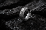 Hammered silver men’s wedding band on wet volcanic stone with dramatic studio lighting.