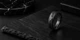 Black hammered wedding ring displayed on dark stone with rugged luxury jewellery styling.