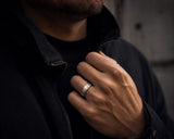 Man wearing a hammered silver and gold wedding ring with dark modern clothing in an urban lifestyle setting.