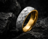 Close-up macro photograph of a hammered silver and gold men’s wedding ring on charcoal slate showing detailed craftsmanship and textured finish.