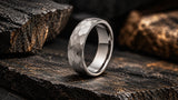 Silver hammered tungsten wedding ring on dark stone with warm gold highlights