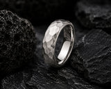 Macro photograph of a hammered silver tungsten wedding band resting on volcanic rock with detailed industrial texture and cinematic shadows