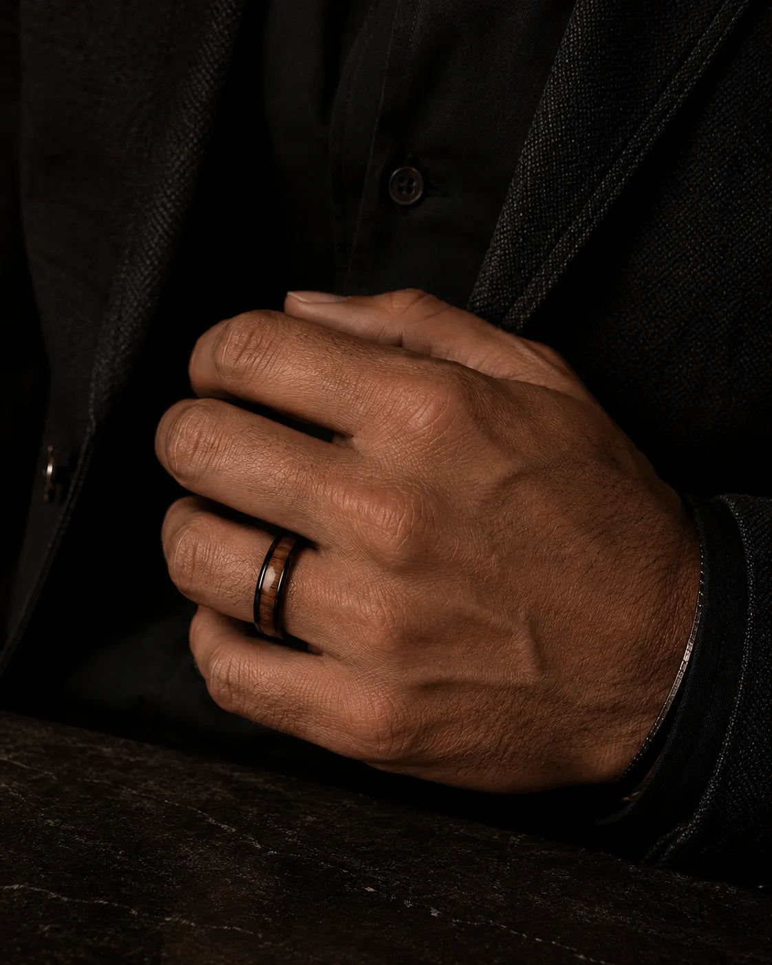 Man wearing a black and reddish-brown wood inlay ring with a dark tailored jacket.