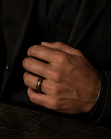 Man wearing a black and reddish-brown wood inlay ring with a dark tailored jacket.