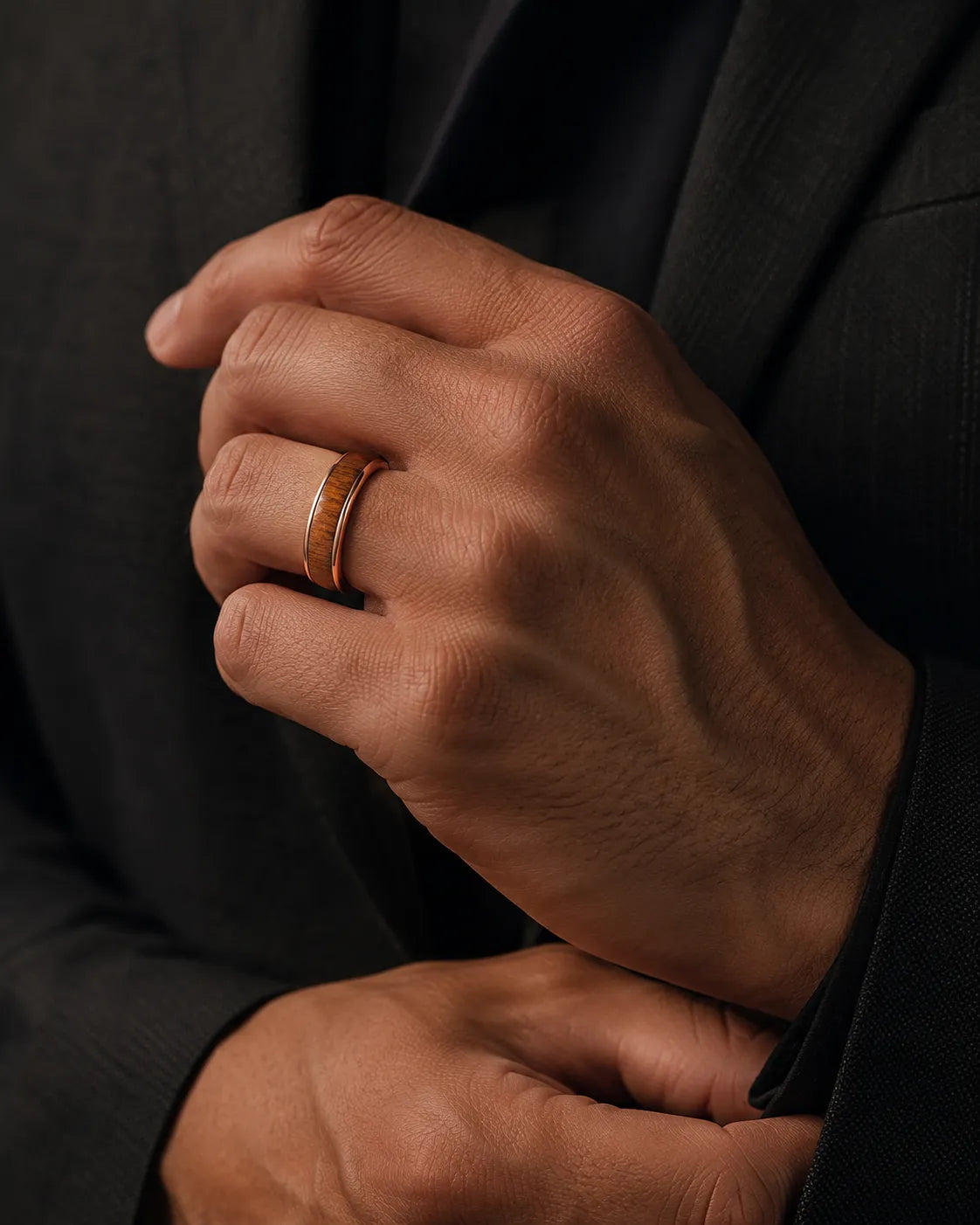 Man wearing a rose gold and reddish-brown wood inlay ring with a dark tailored jacket.
