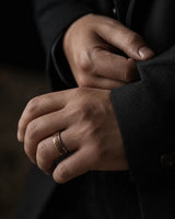 Man wearing a silver and reddish-brown wood inlay ring with a dark tailored jacket.