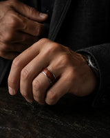 Man wearing a silver and reddish-brown wood inlay ring with a dark tailored jacket.