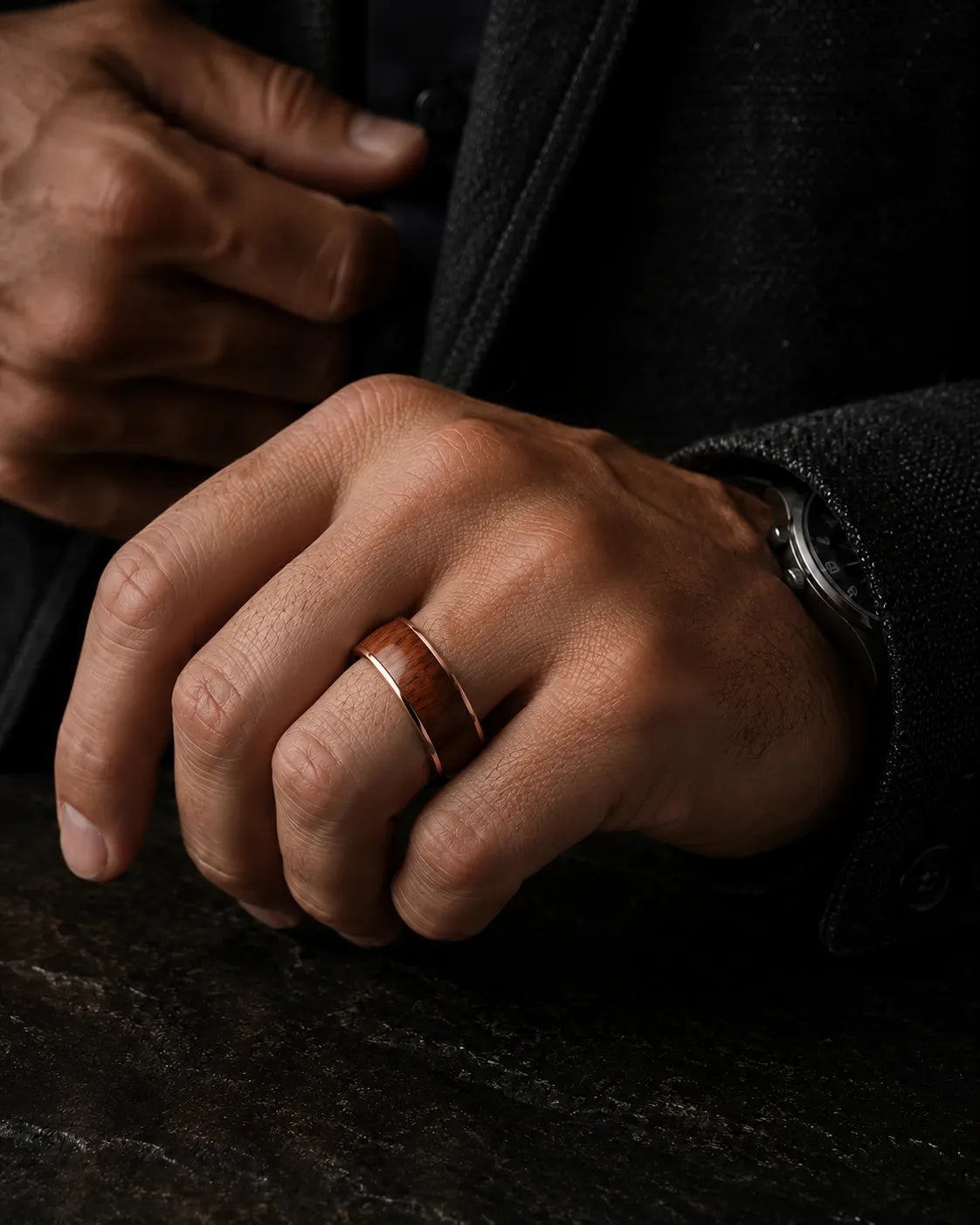Man wearing a rose gold and reddish-brown wood inlay ring with a dark tailored jacket.