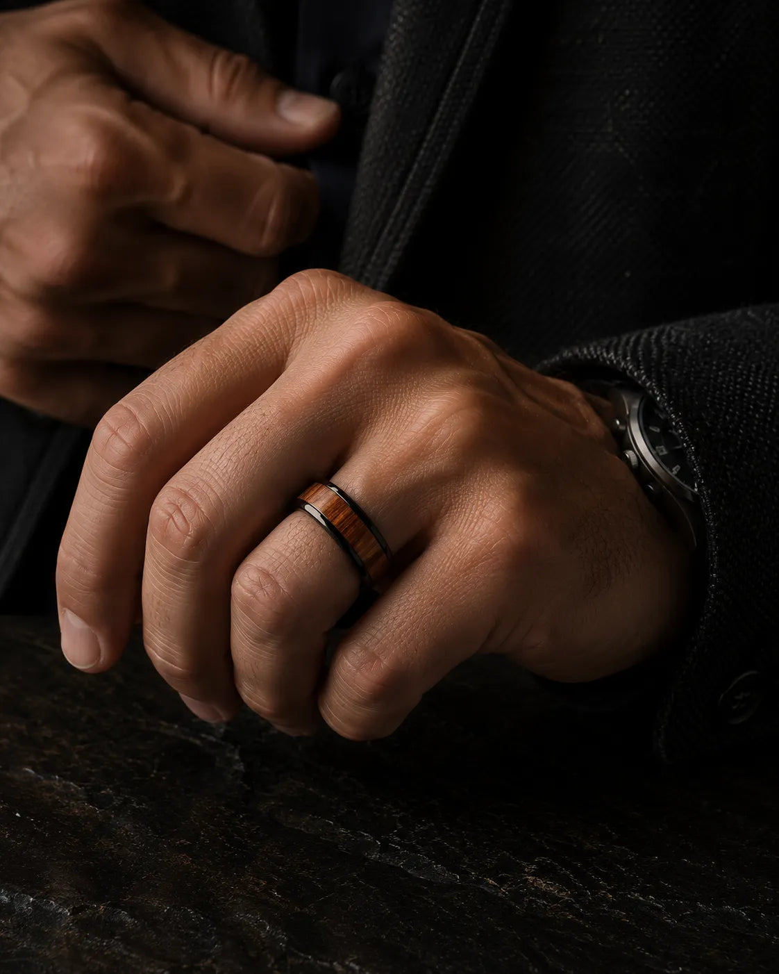 Man wearing a black and reddish-brown wood inlay ring with a dark tailored jacket.