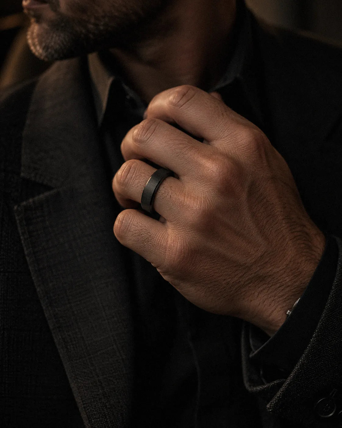 Man wearing a black brushed tungsten wedding ring while adjusting a dark tailored jacket.