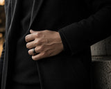 Man wearing a black woodland-inspired wedding ring with engraved forest detailing and wood interior in a dark luxury lifestyle setting.