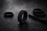 Black silicone men’s wedding ring on a dark textured athletic-inspired background with moody luxury lighting