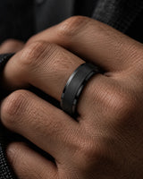 Close-up of a man wearing a black titanium wedding ring with a brushed centre and polished stepped edges.