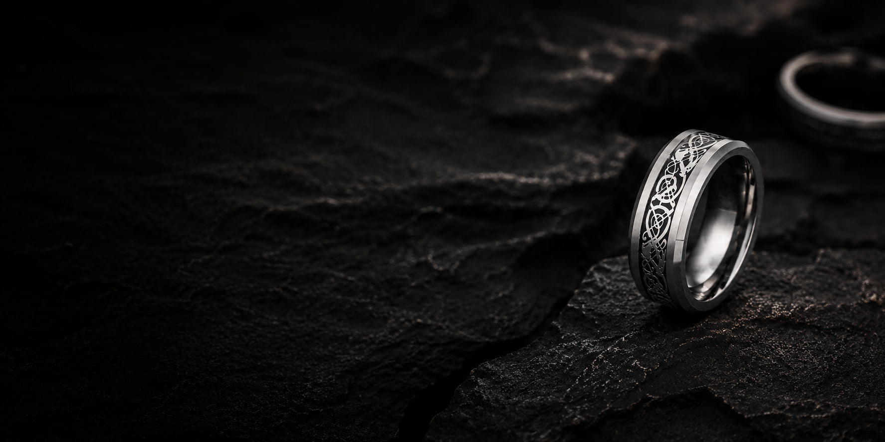 Luxury men’s Celtic wedding ring collection banner featuring a silver engraved ring against dark charcoal stone textures with moody cinematic lighting.