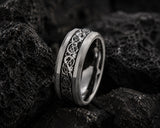 Macro close-up of a silver Celtic pattern men’s wedding ring resting amongst rugged volcanic rock with detailed texture and moody luxury lighting.
