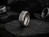 Silver Celtic men’s wedding ring with black engraved pattern resting on dark volcanic rock in a cinematic luxury ecommerce hero image.