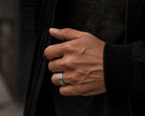Man wearing a silver Celtic engraved wedding ring with polished edges in a dark luxury lifestyle setting with cinematic masculine styling.