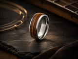 Silver tungsten guitar string wedding ring with reclaimed wood inlay on warm moody wood background for guitar string ring collection