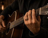Man wearing silver guitar string wedding ring while playing acoustic guitar in warm cinematic lighting