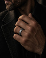 Man wearing a gunmetal grey brushed tungsten wedding ring while adjusting a dark tailored jacket.