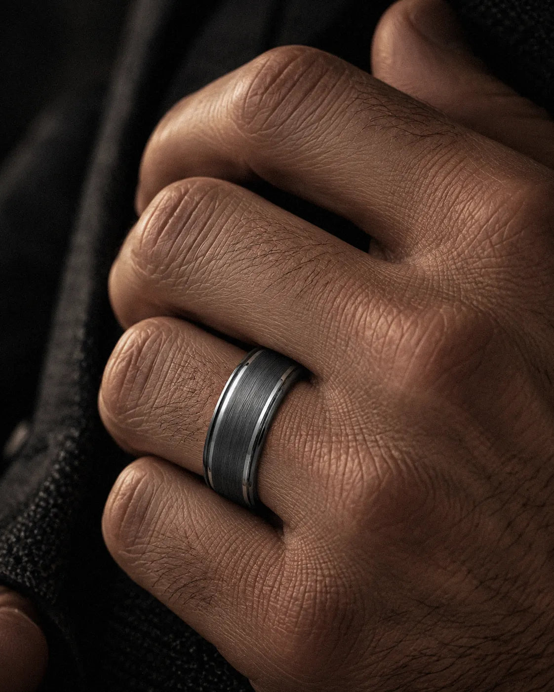 Man wearing a brushed gunmetal wedding ring with polished ridge edges on his ring finger.