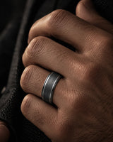 Man wearing a brushed gunmetal wedding ring with polished ridge edges on his ring finger.