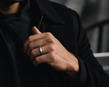 Man wearing a brushed silver and black tungsten wedding ring with dark modern clothing and premium urban aesthetic