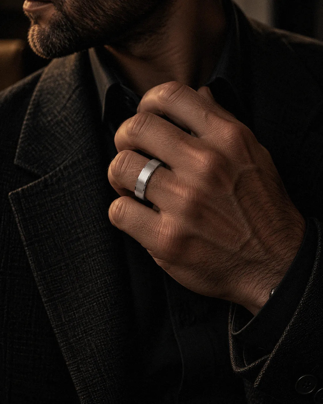 Man wearing a silver brushed tungsten wedding ring while adjusting a dark tailored jacket.