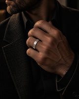 Man wearing a silver brushed tungsten wedding ring while adjusting a dark tailored jacket.