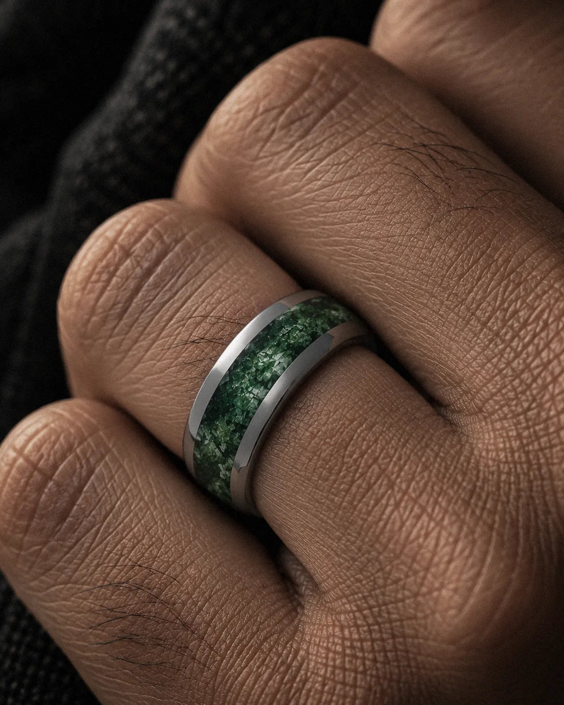 Macro close-up of a silver tungsten wedding ring with green moss agate inlay worn on a man’s hand