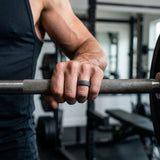 Person holding a barbell with a blurred gym background wearing a slate silicone ring